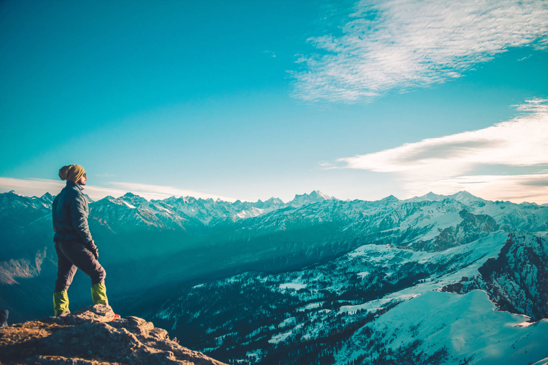 A Person Standing On Top Of A Mountain Looking At The Snowy Mountains Background