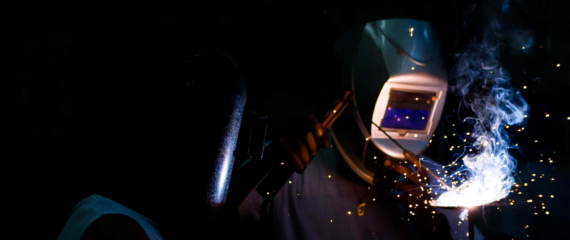 A Person Welding With A Torch And Sparks Background