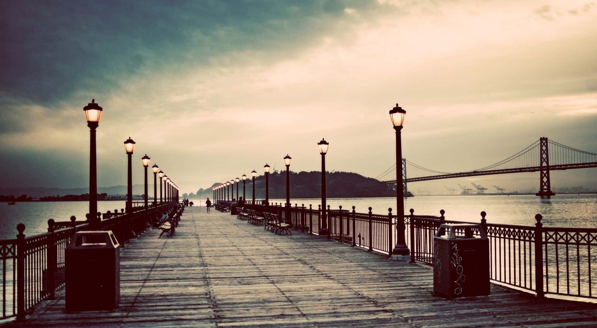 A Pier With Benches And A Bridge In The Background Background