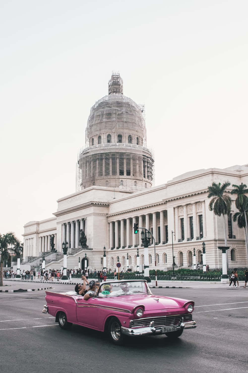 A Pink Convertible Driving Down The Street In Front Of A Building Background