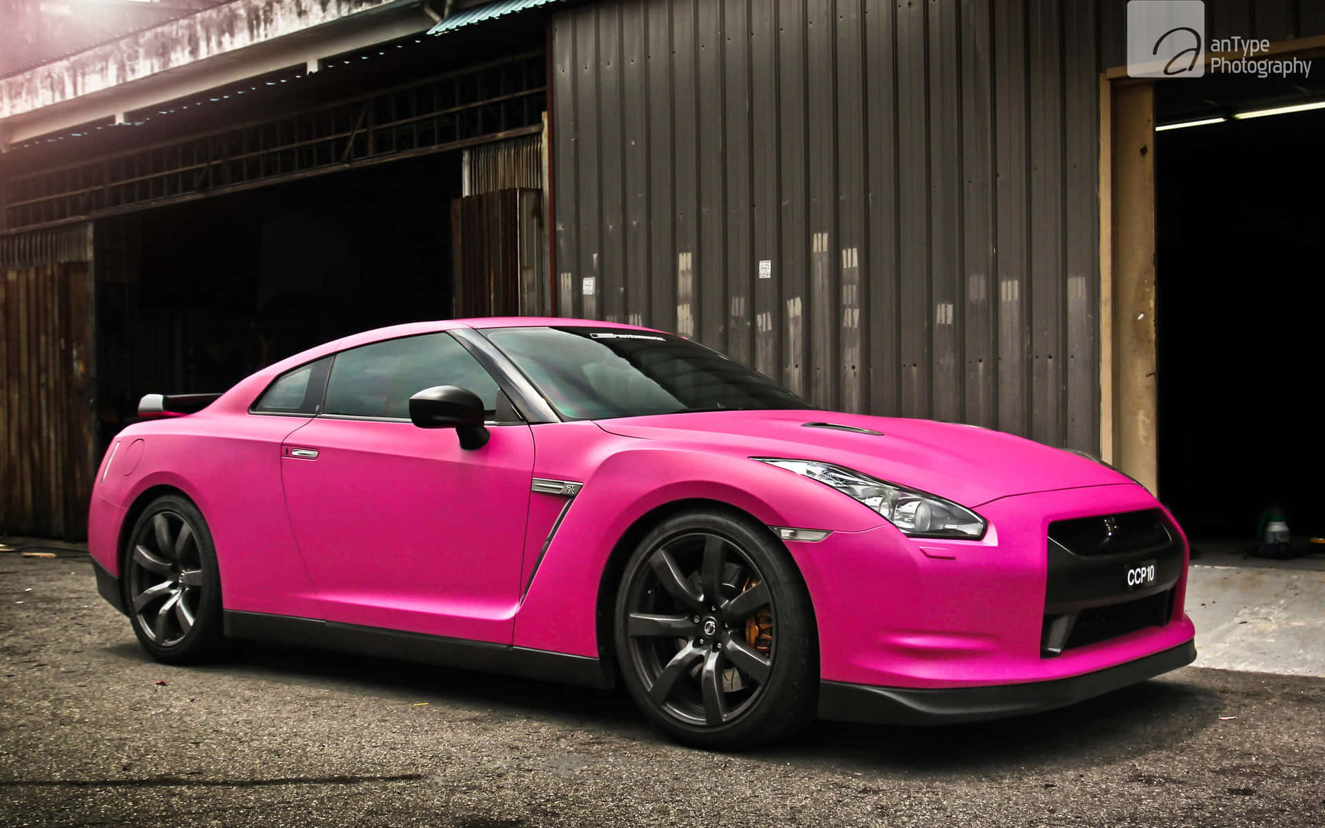 A Pink Nissan Gtr Parked In Front Of A Garage Background