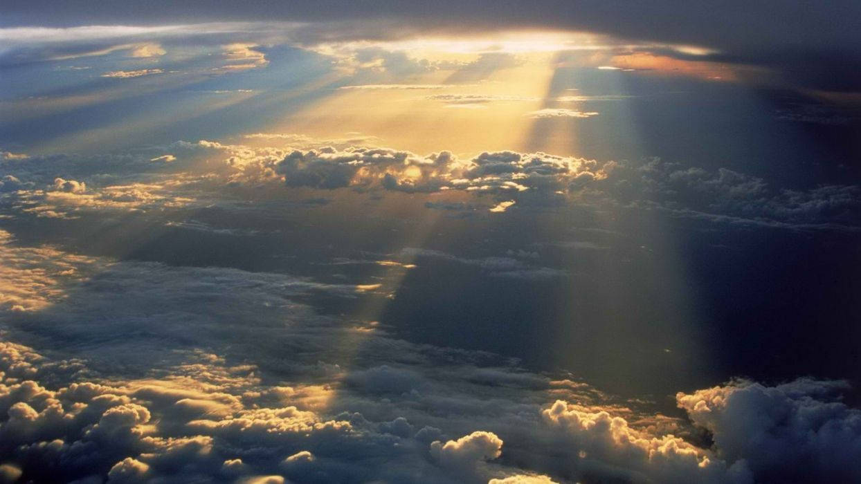 A Plane Flying Over Clouds With Sun Beams Shining Through Background