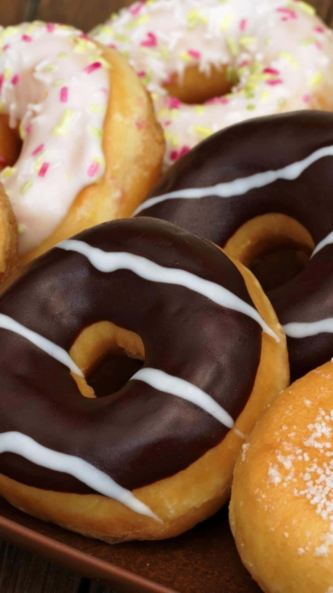 A Plate Of Donuts With Frosting And Sprinkles Background