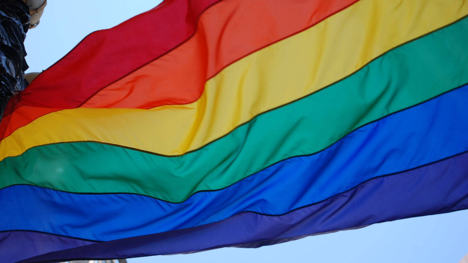 A Rainbow Flag Is Flying In The Wind Background