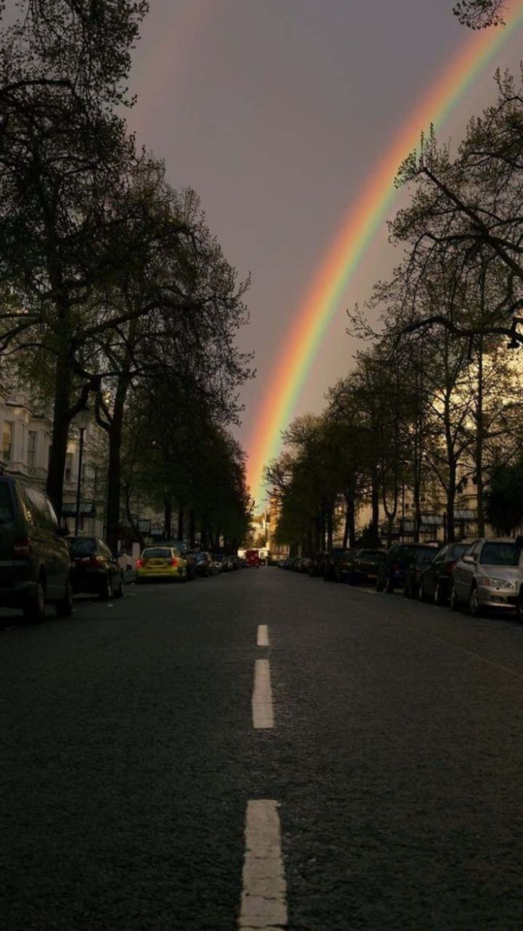 A Rainbow Is Seen Over A Street With Cars Parked In The Street Background