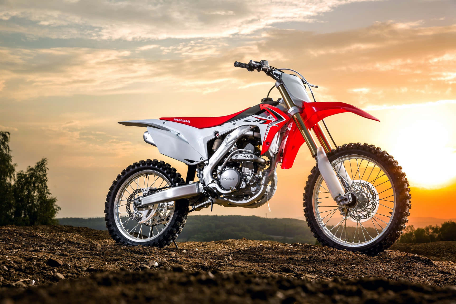 A Red And White Dirt Bike Is Parked On A Dirt Road Background