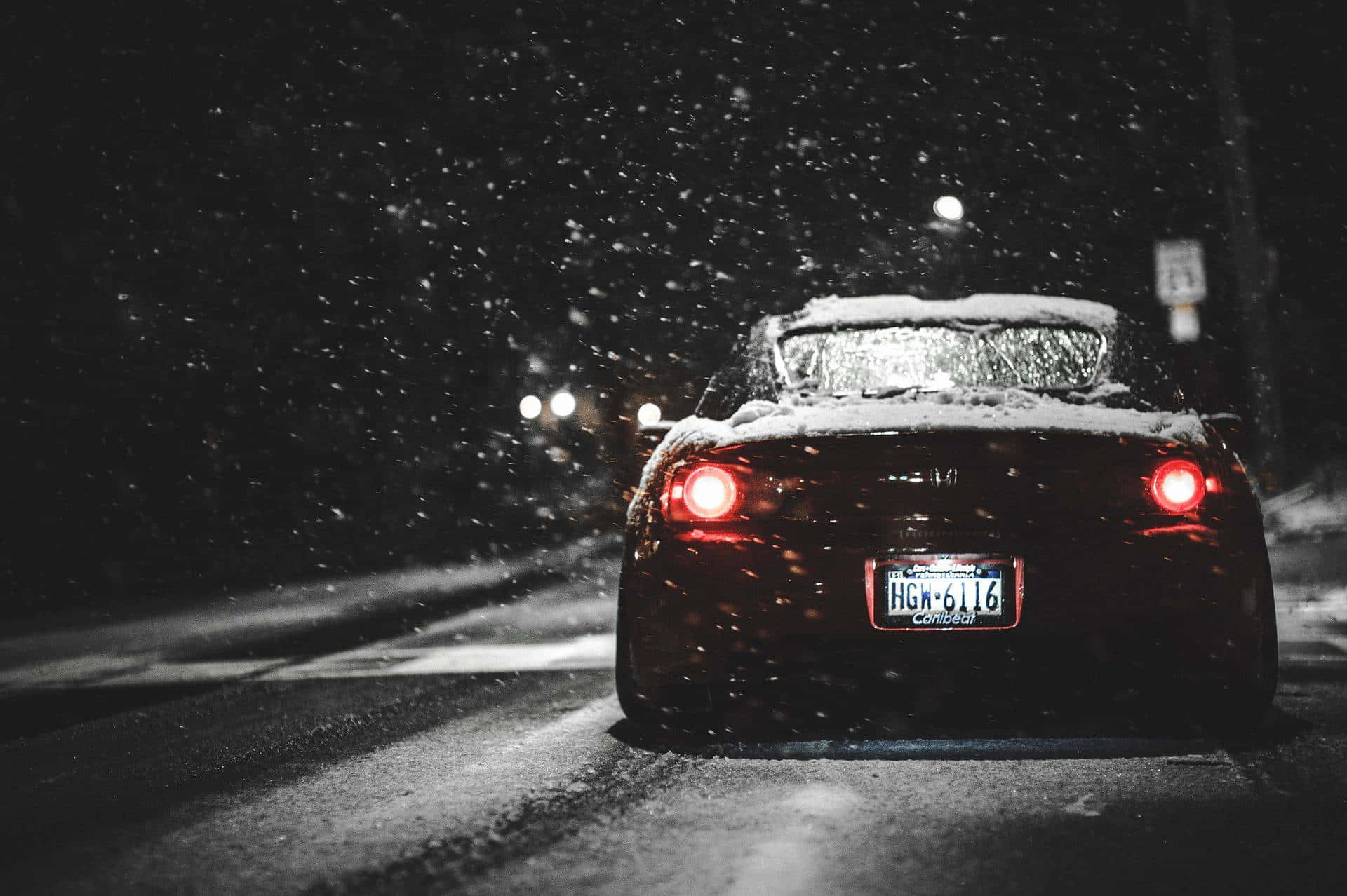 A Red Car Driving Down A Snowy Street At Night Background