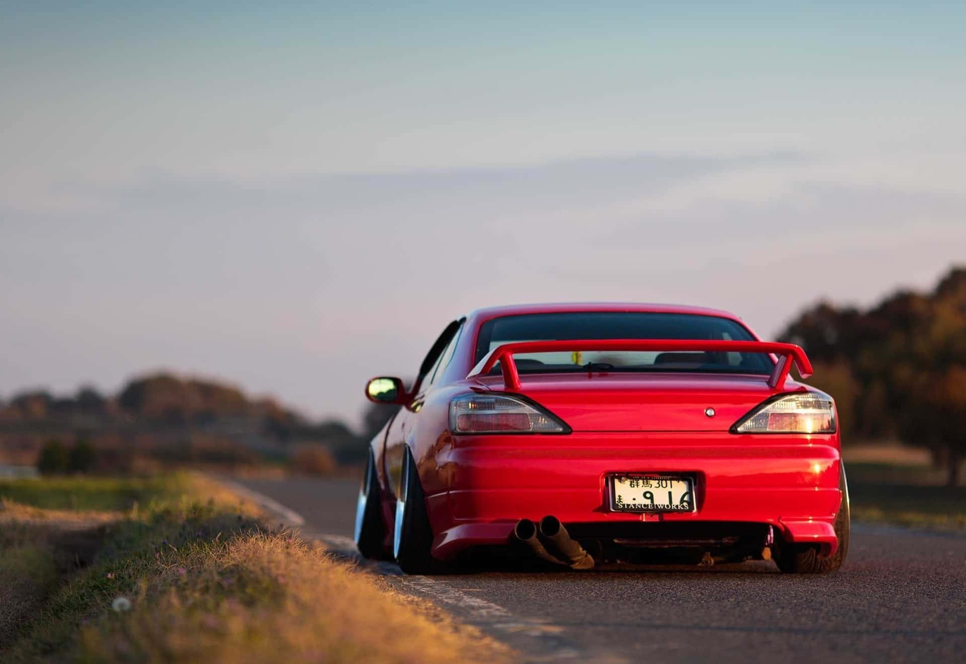 A Red Car Is Parked On A Country Road Background