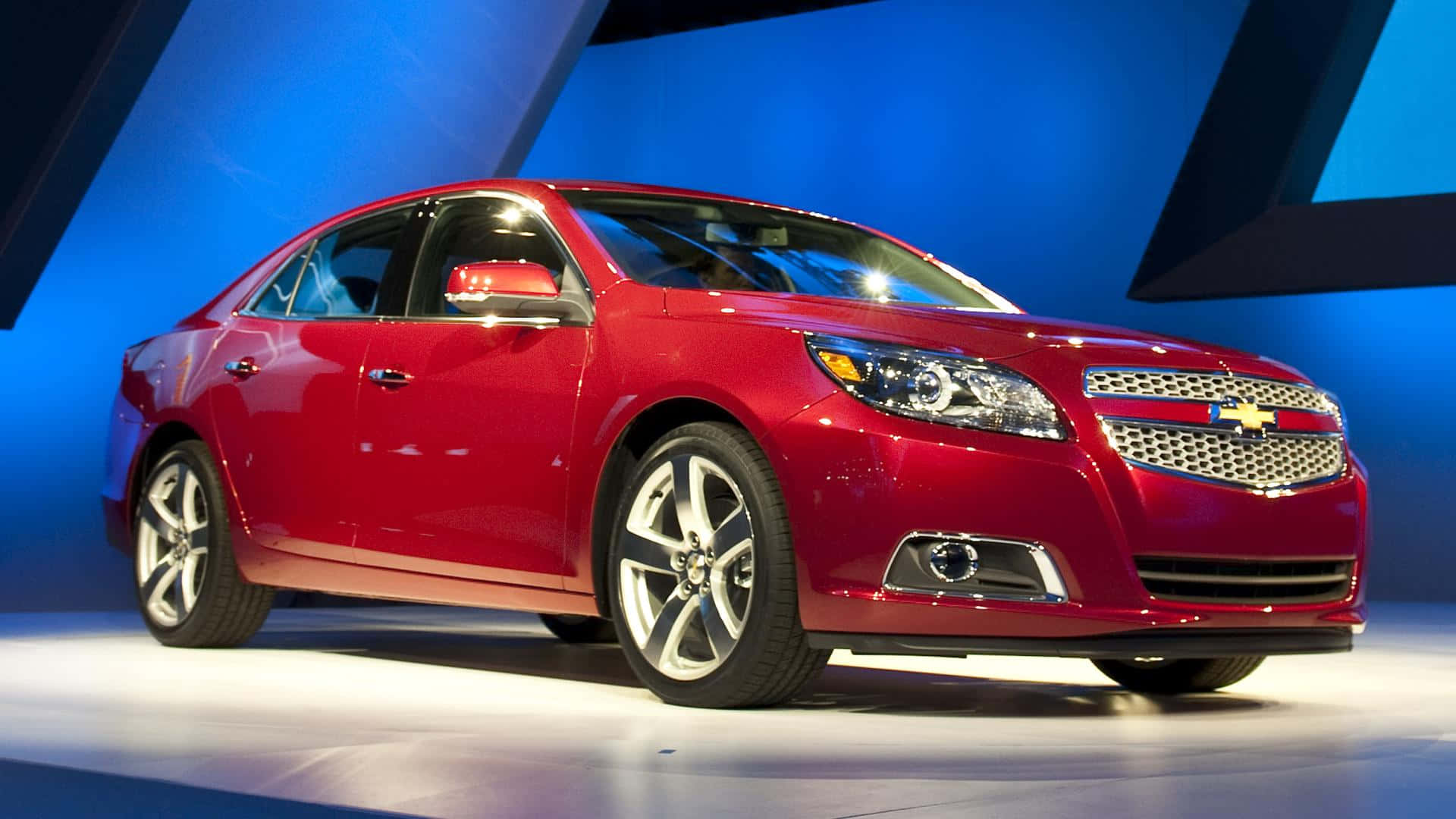 A Red Chevrolet Malibu Is On Display At An Auto Show Background