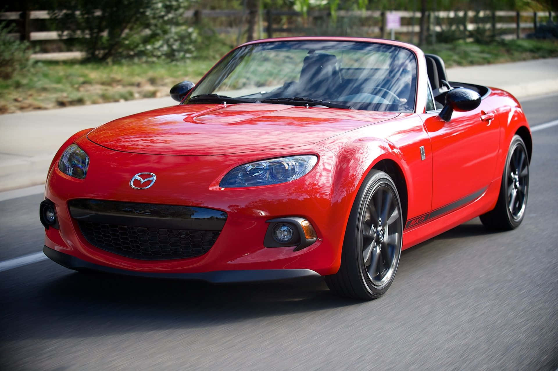 A Red Mazda Mx-5 Roadster Driving Down The Road Background