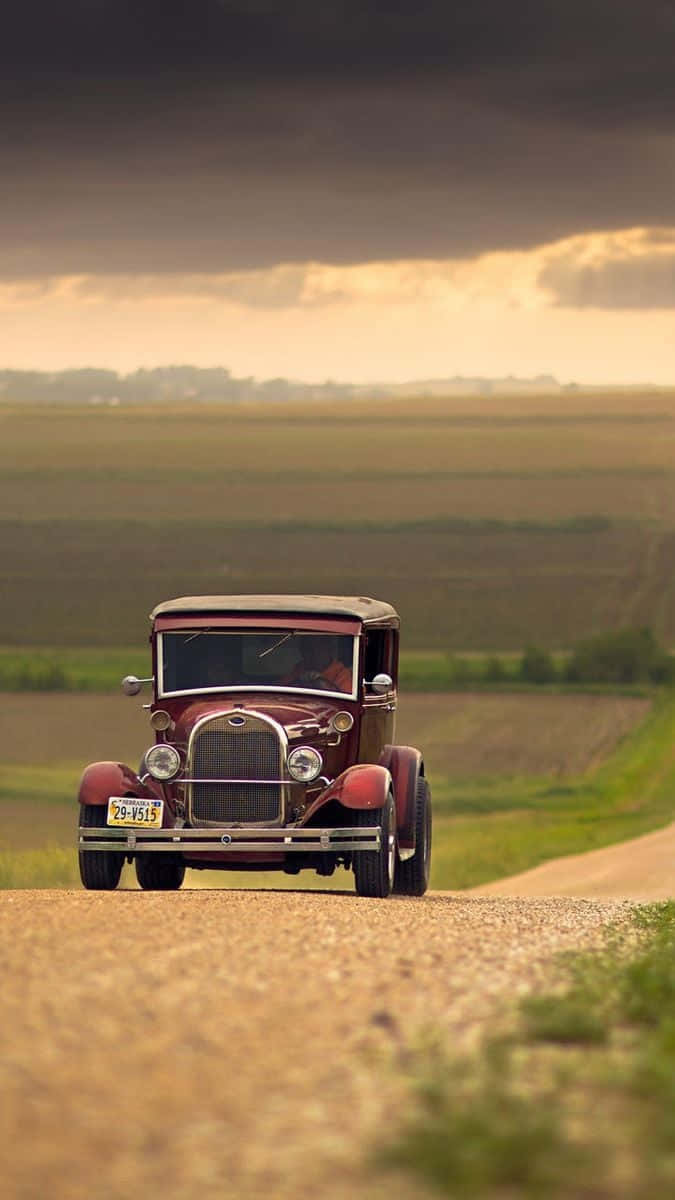 A Red Old Car Driving Down A Dirt Road