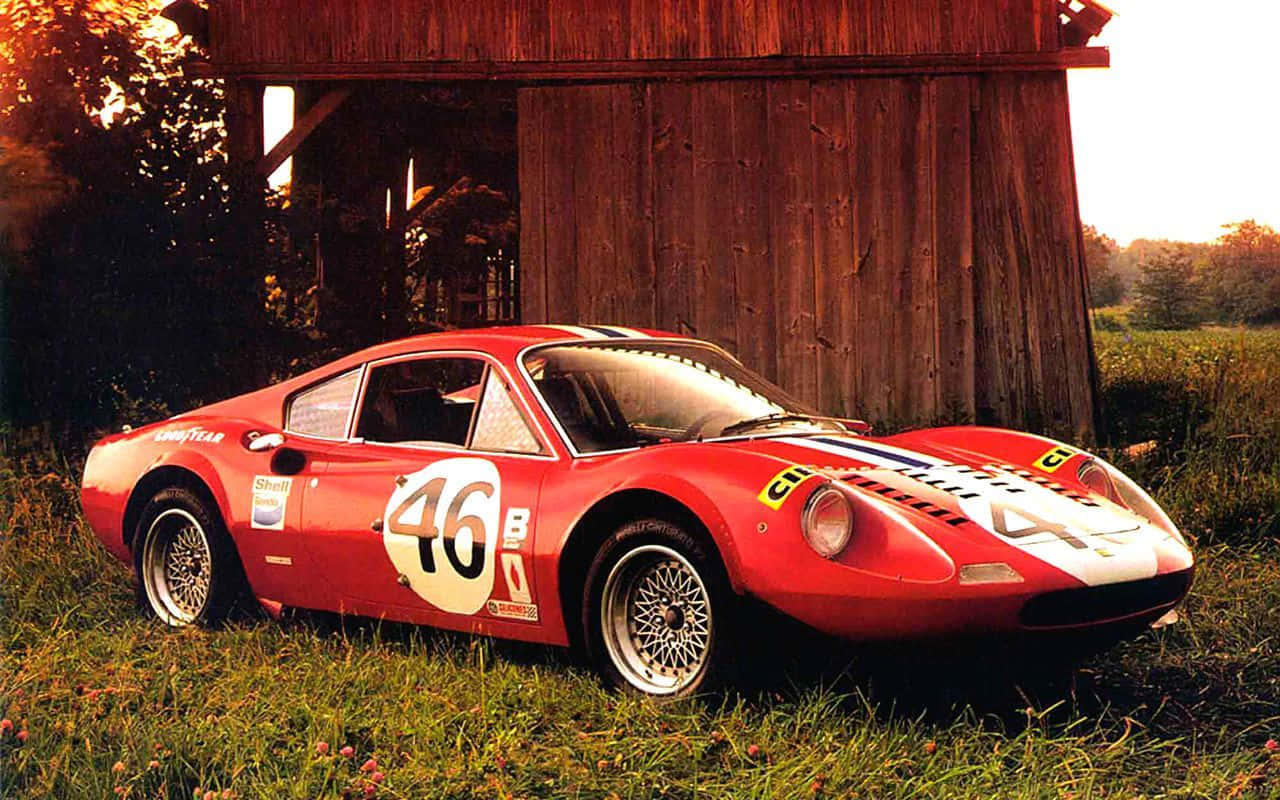 A Red Race Car Parked In Front Of A Barn Background