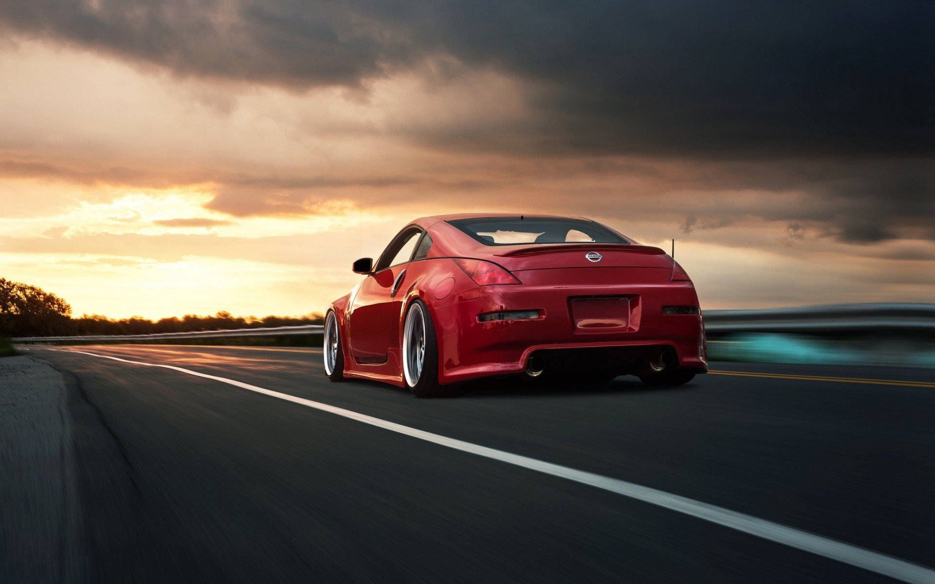 A Red Sports Car Driving Down A Road At Sunset