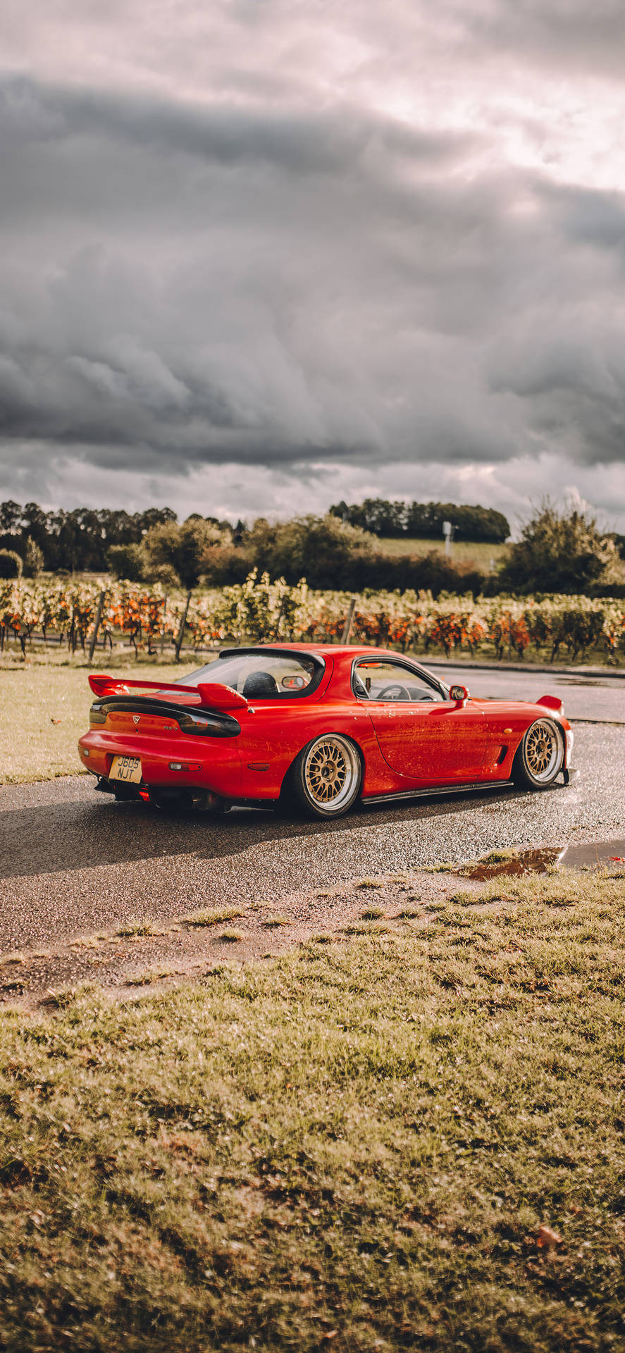 A Red Sports Car Driving Down A Road Background