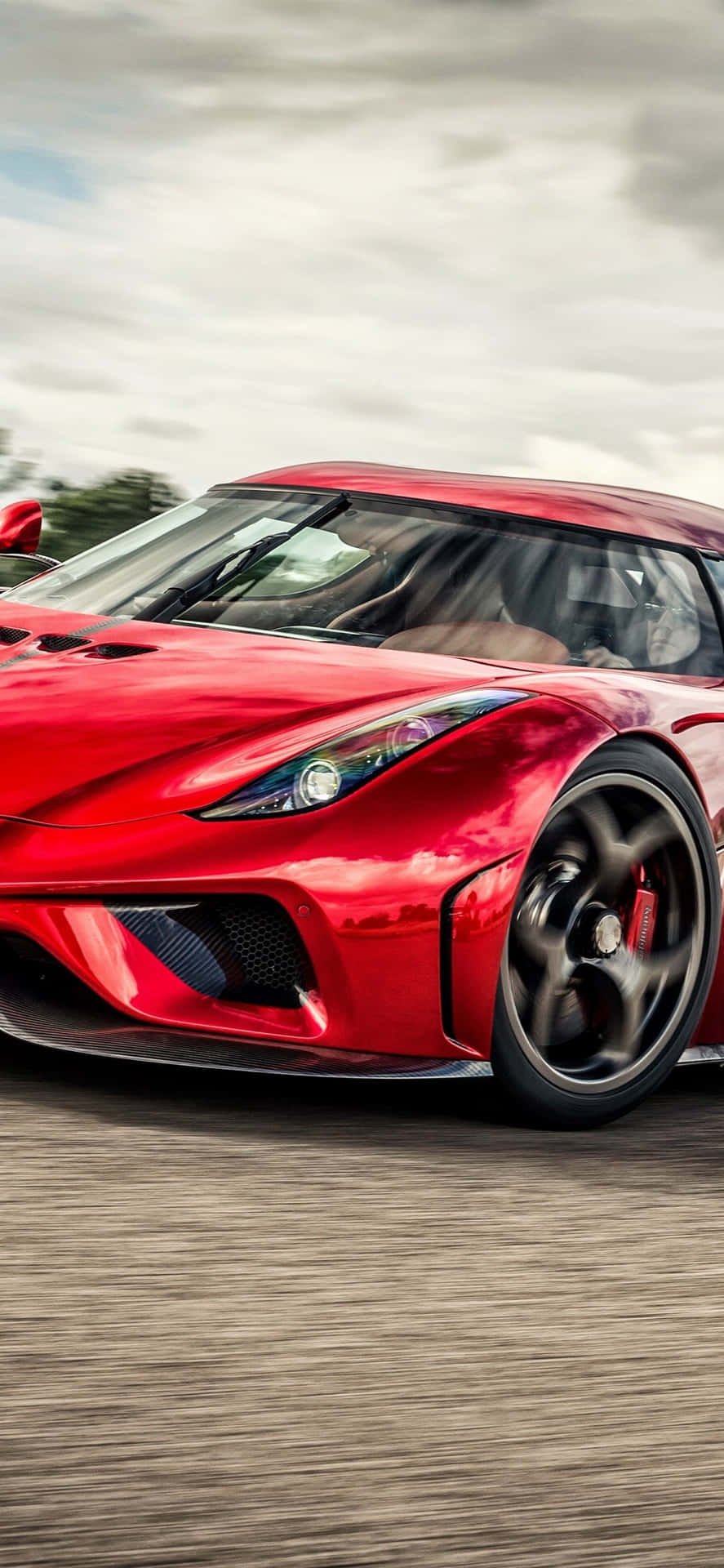 A Red Sports Car Is Driving Down A Road Background