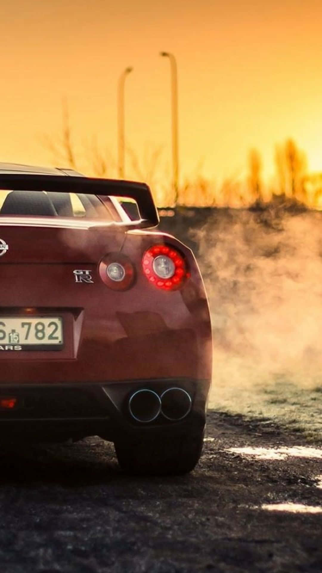 A Red Sports Car Is Driving Down The Road At Sunset Background