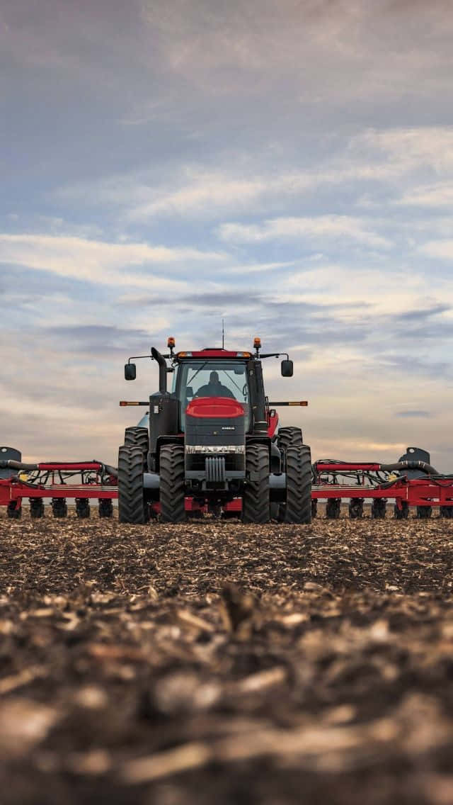 A Red Tractor Is Parked In A Field Background