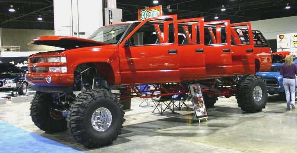 A Red Truck With Large Tires On Display At A Show Background