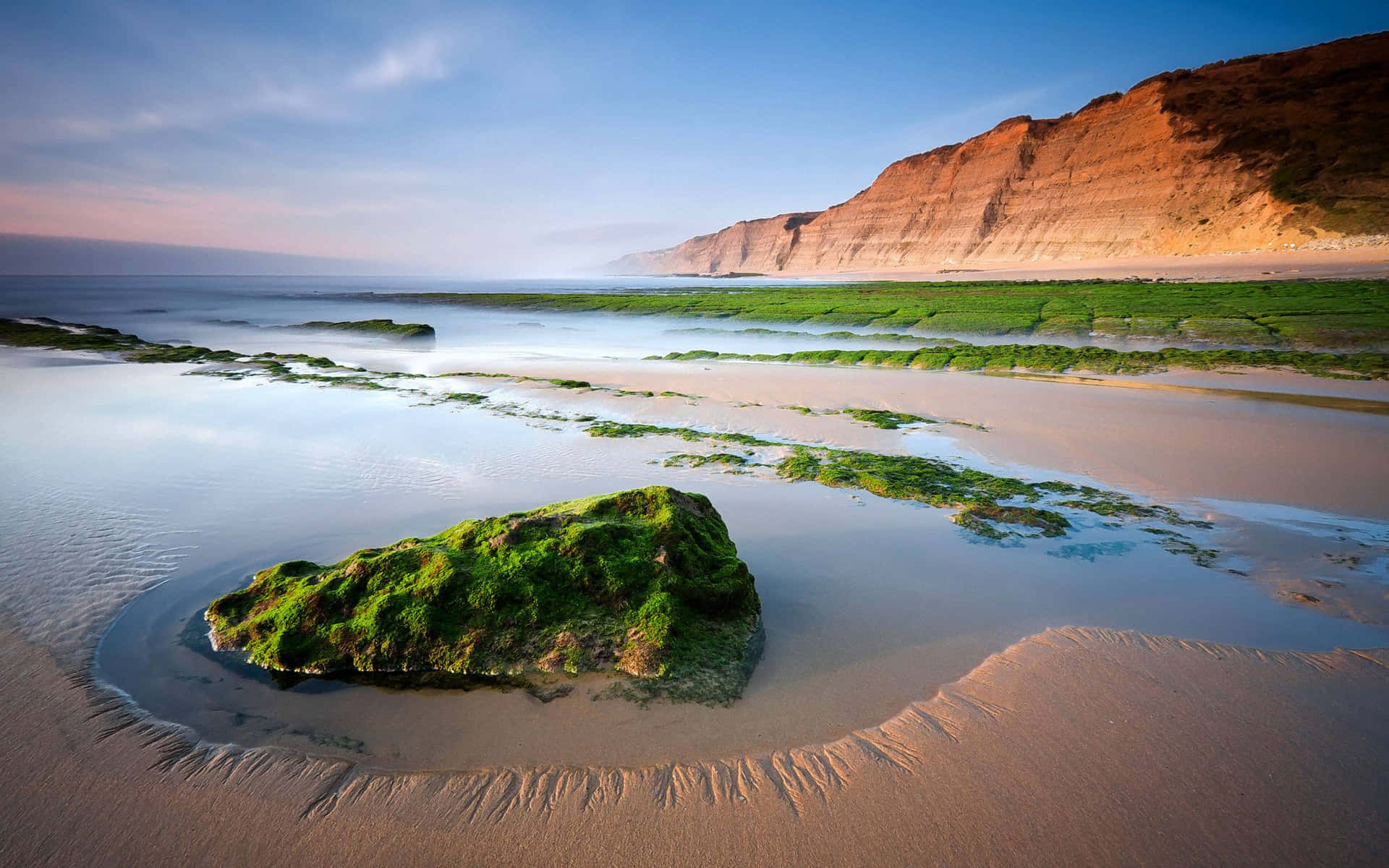 A Rock On The Beach With A Cliff In The Background Background