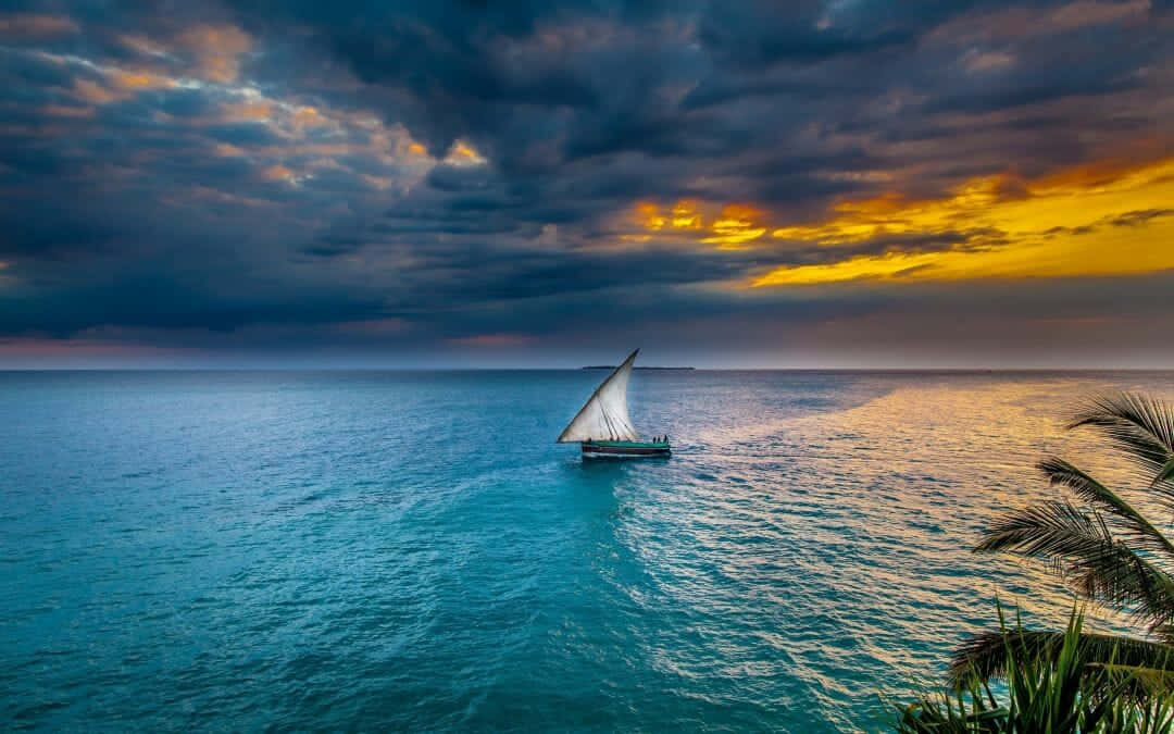 A Sailboat Sails In The Ocean At Sunset Background