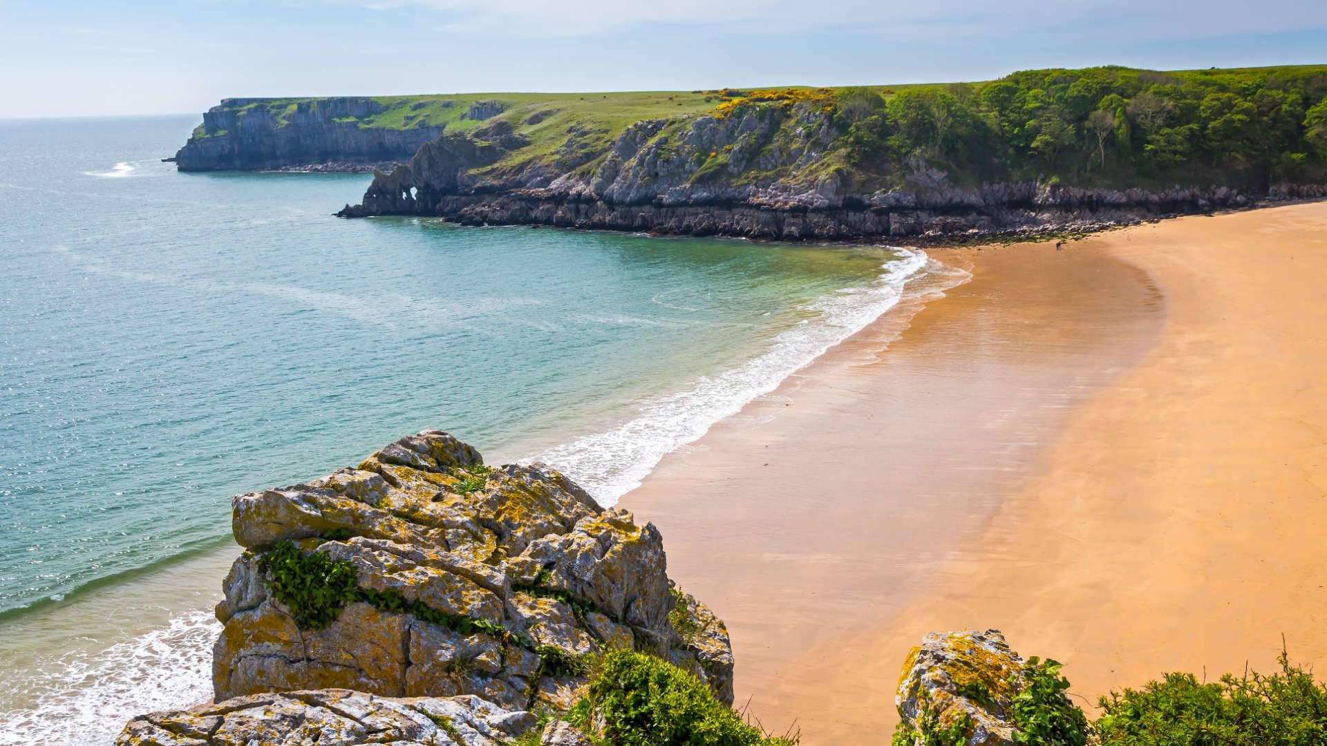 A Sandy Beach With A Cliff And Ocean Background