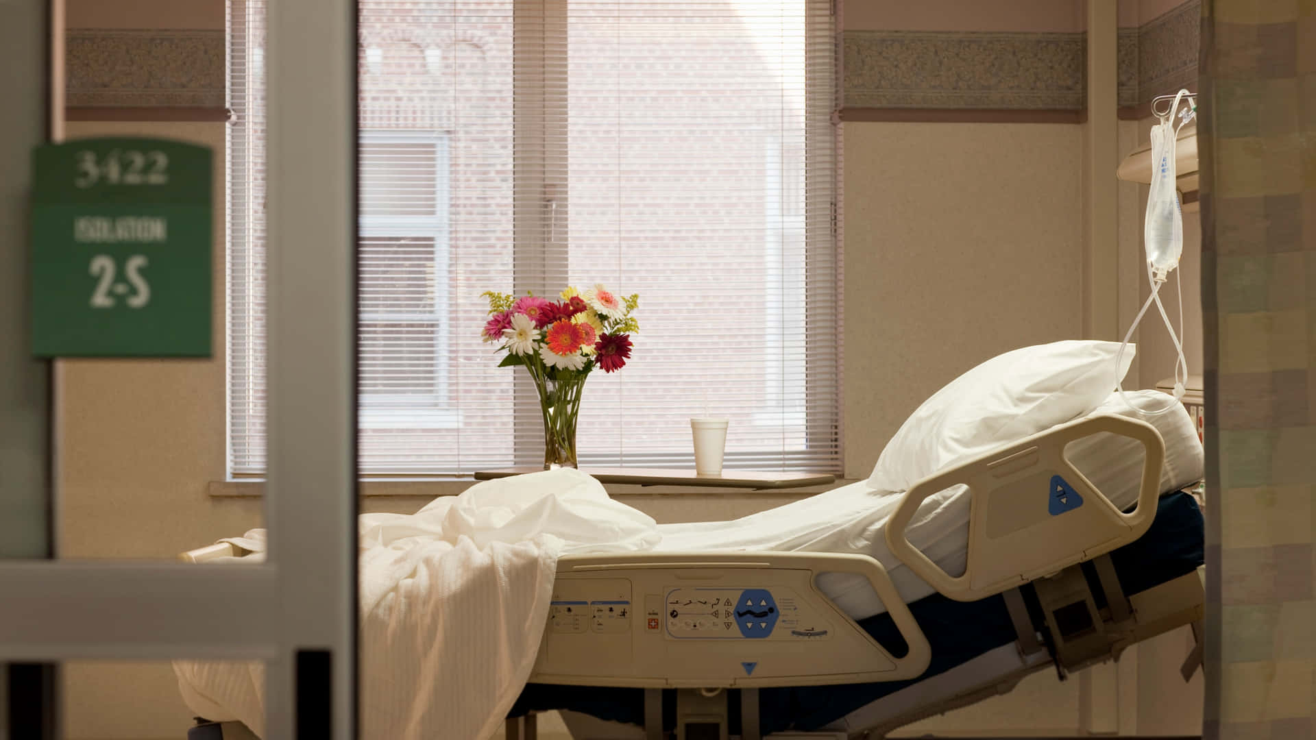 A Serene Hospital Room Featuring A Clean Hospital Bed And A Flower Vase By The Bedside.