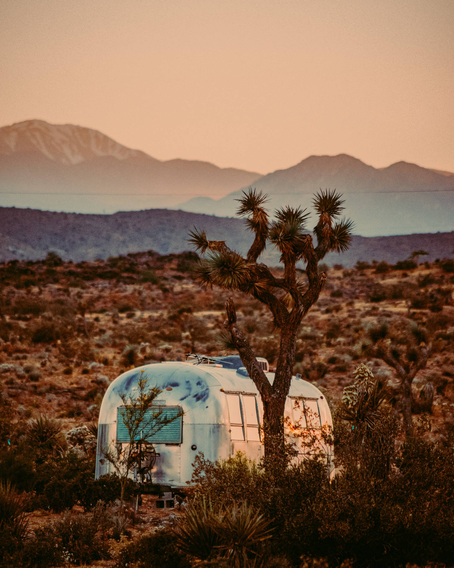 A Silver Airstream Sits In The Desert At Sunset Background