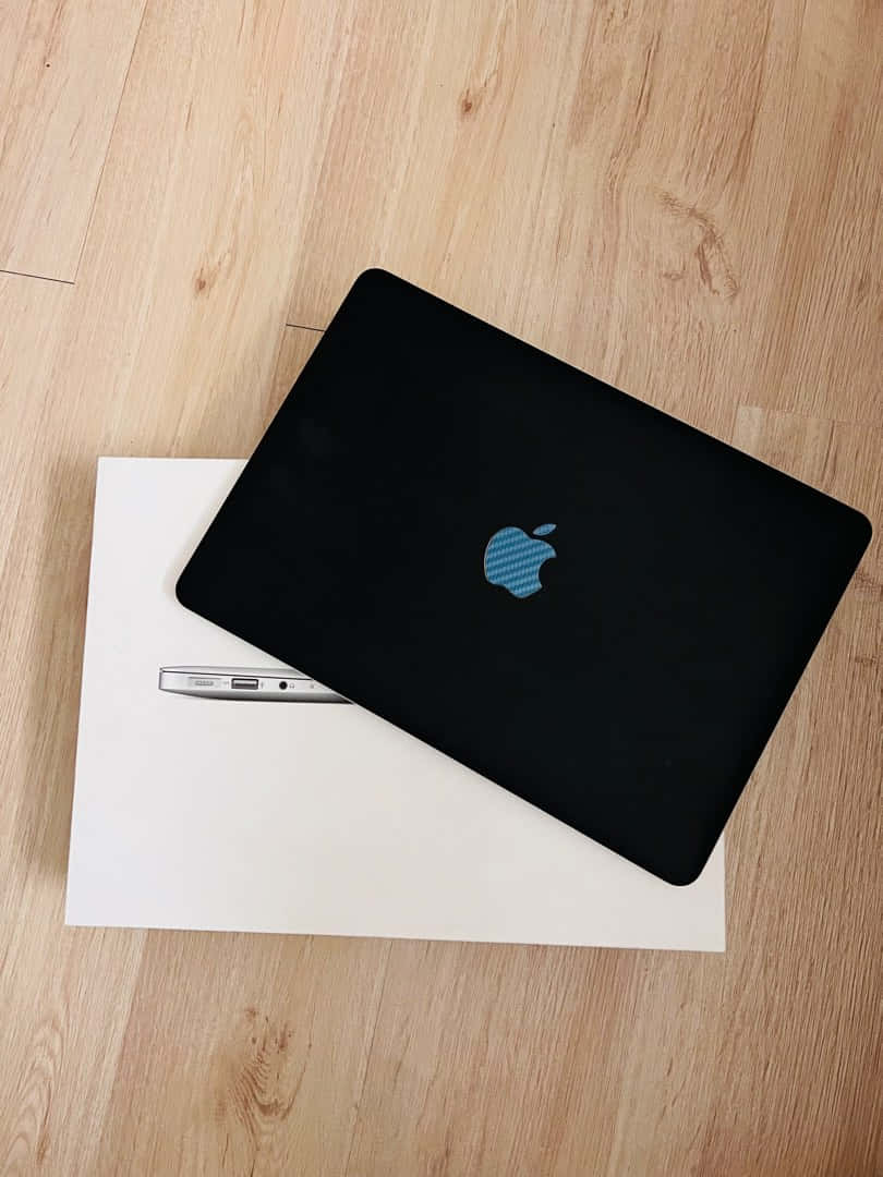 A Sleek Black Macbook Sitting On A White Desk Background