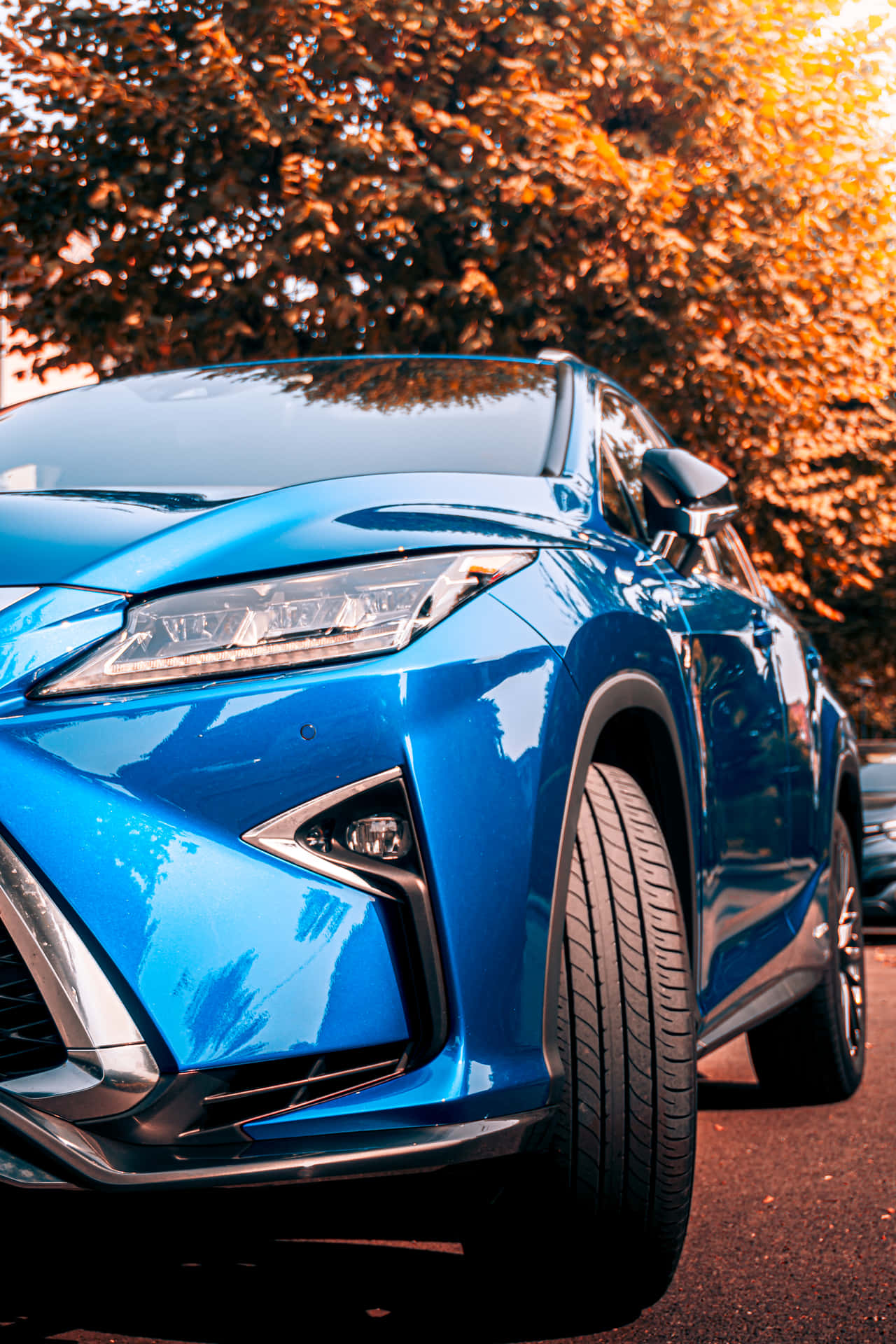 A Sleek Blue Car Parked On The Street With A Beautiful Backdrop.