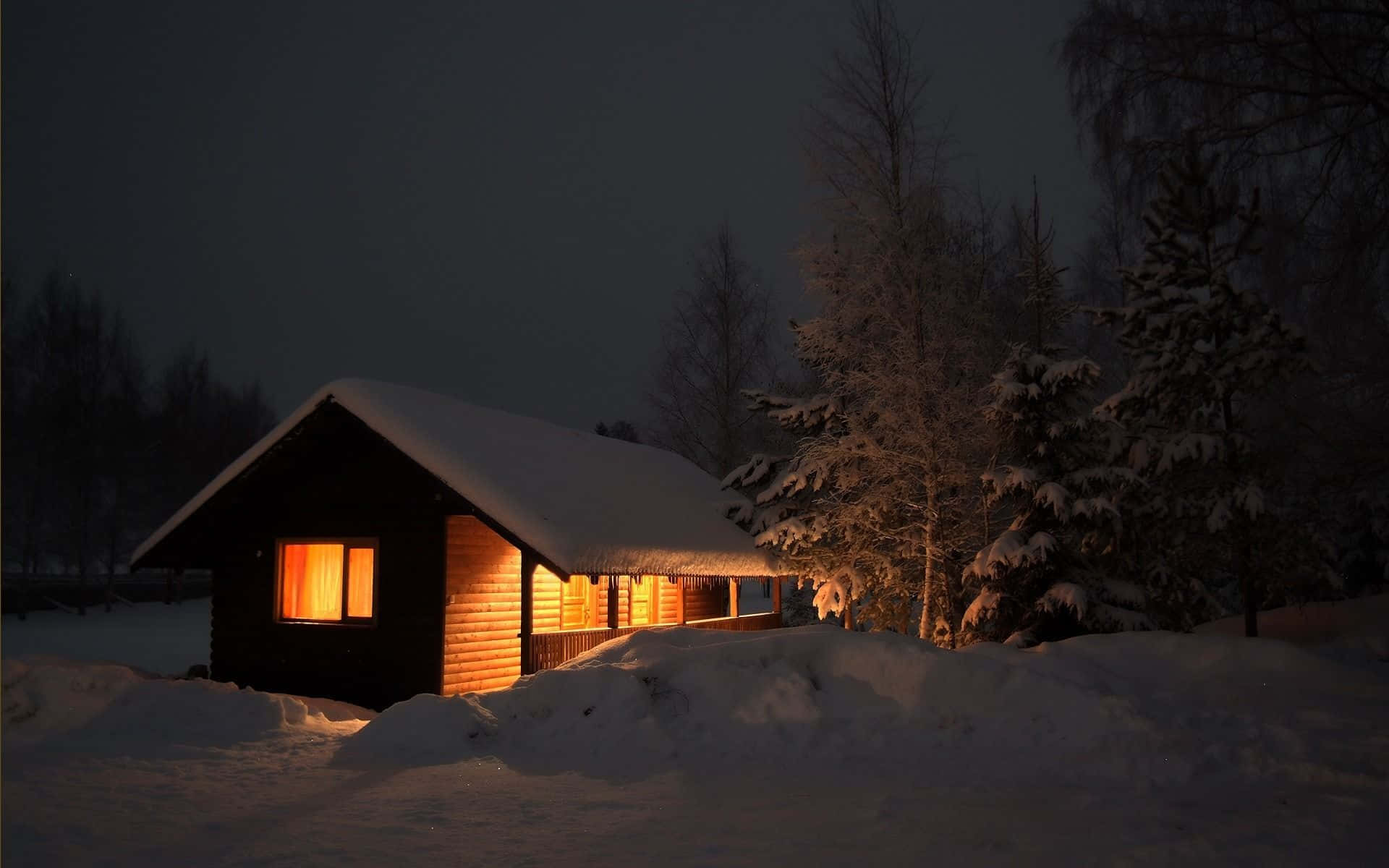 A Small Cabin Lit Up At Night In The Snow