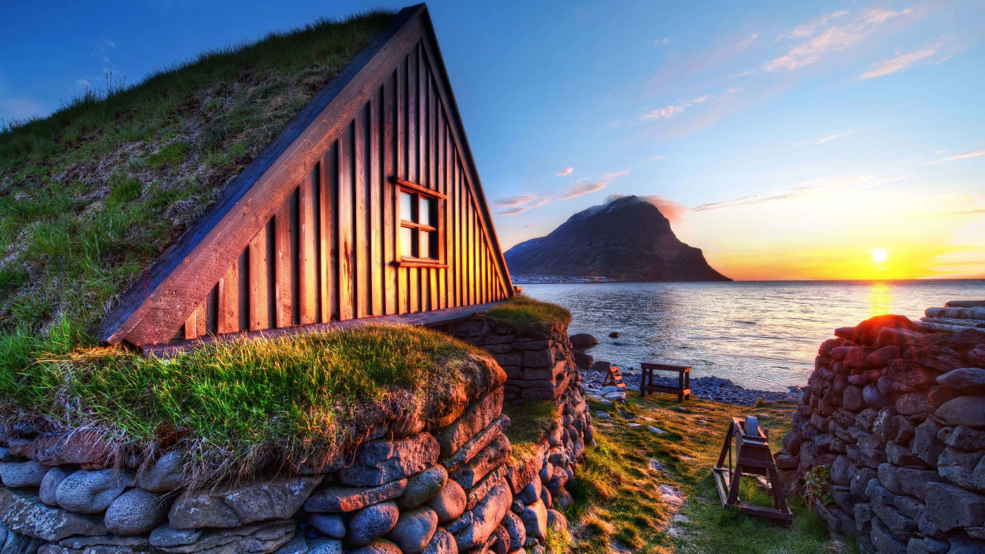 A Small Cottage With Grass On The Side Of The Ocean Background