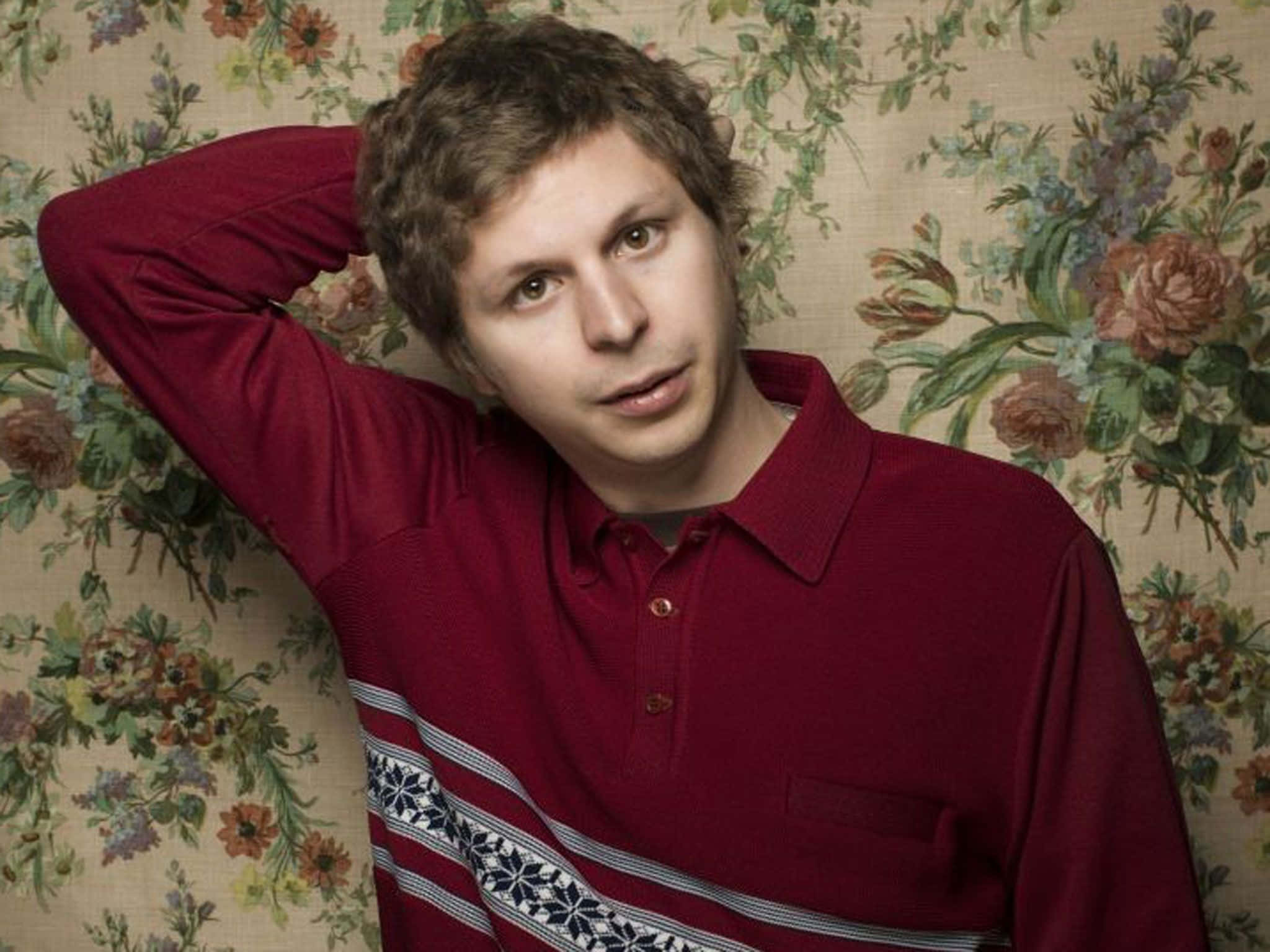 A Smiling Michael Cera Amid A Colorful, Abstract Background.