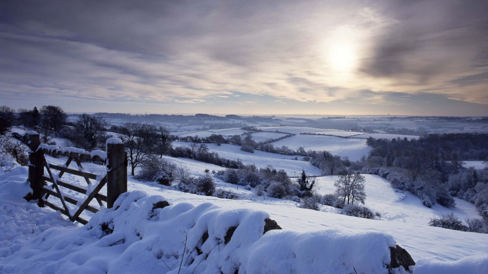 A Snow Covered Field With A Fence And Sun Background