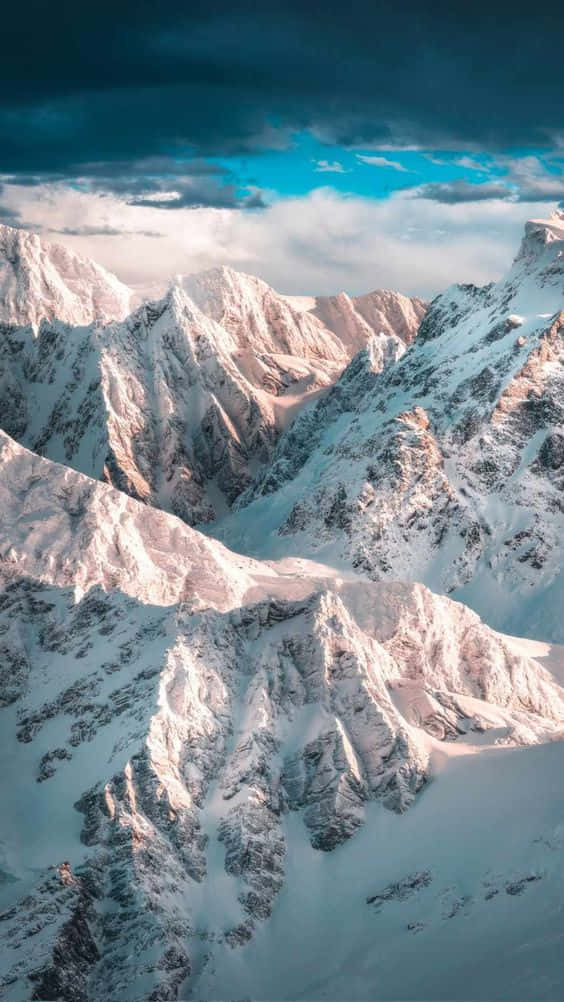 A Snow Covered Mountain Range With Clouds In The Sky Background