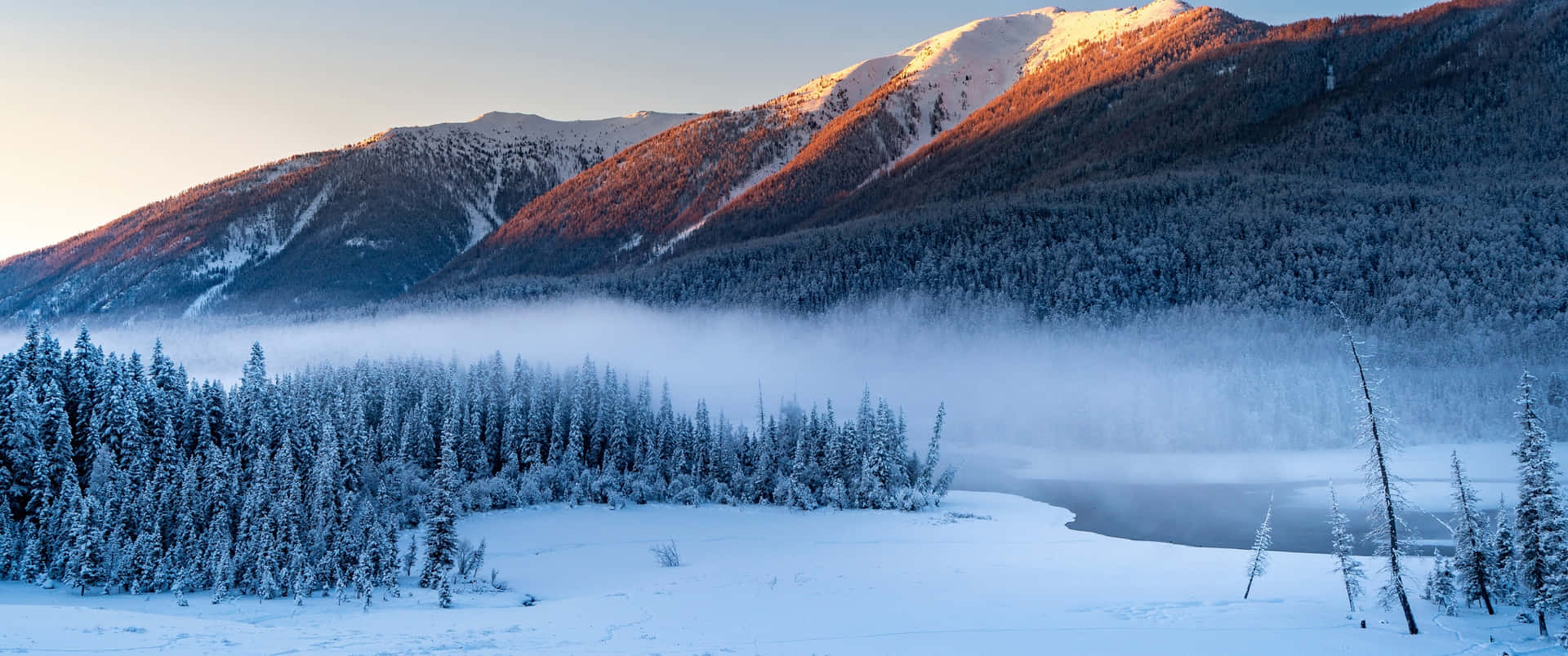 A Snow Covered Mountain Range With Trees And A Lake