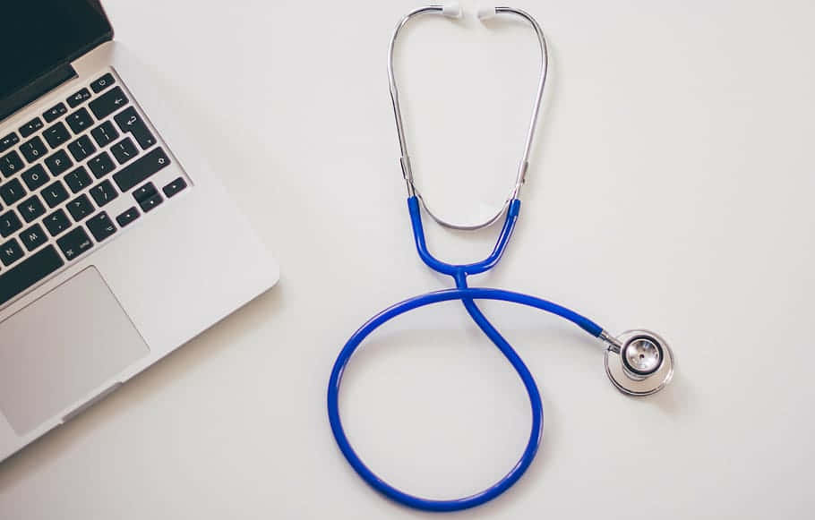 A Stethoscope Next To A Laptop And A Laptop Background