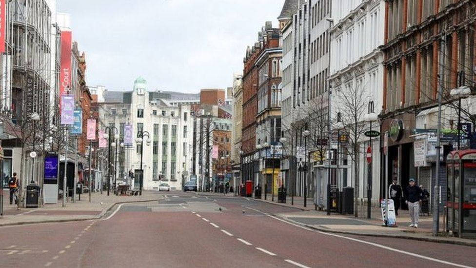 A Street With Buildings And People Walking Down It