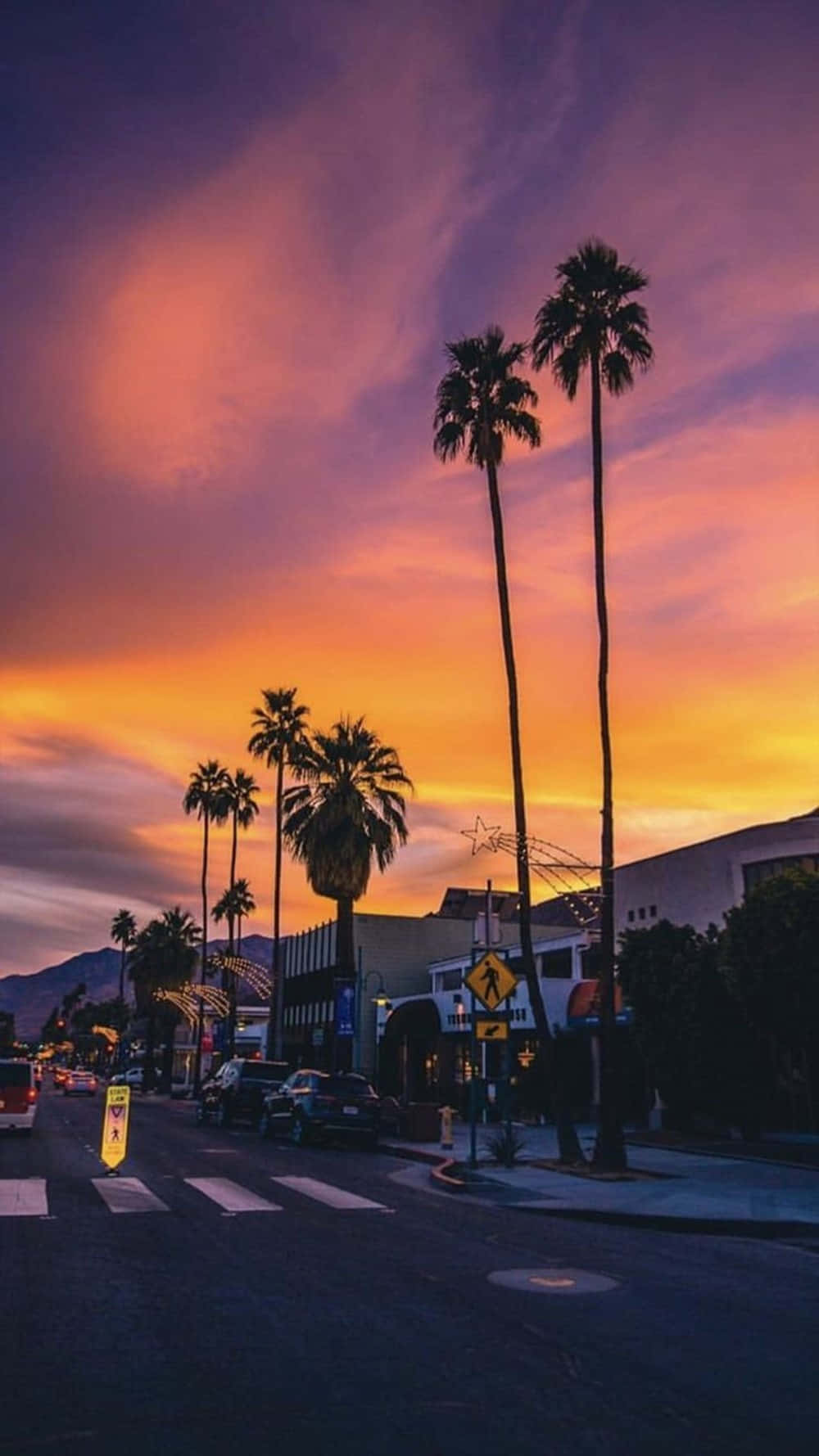 A Street With Palm Trees And A Sunset Background