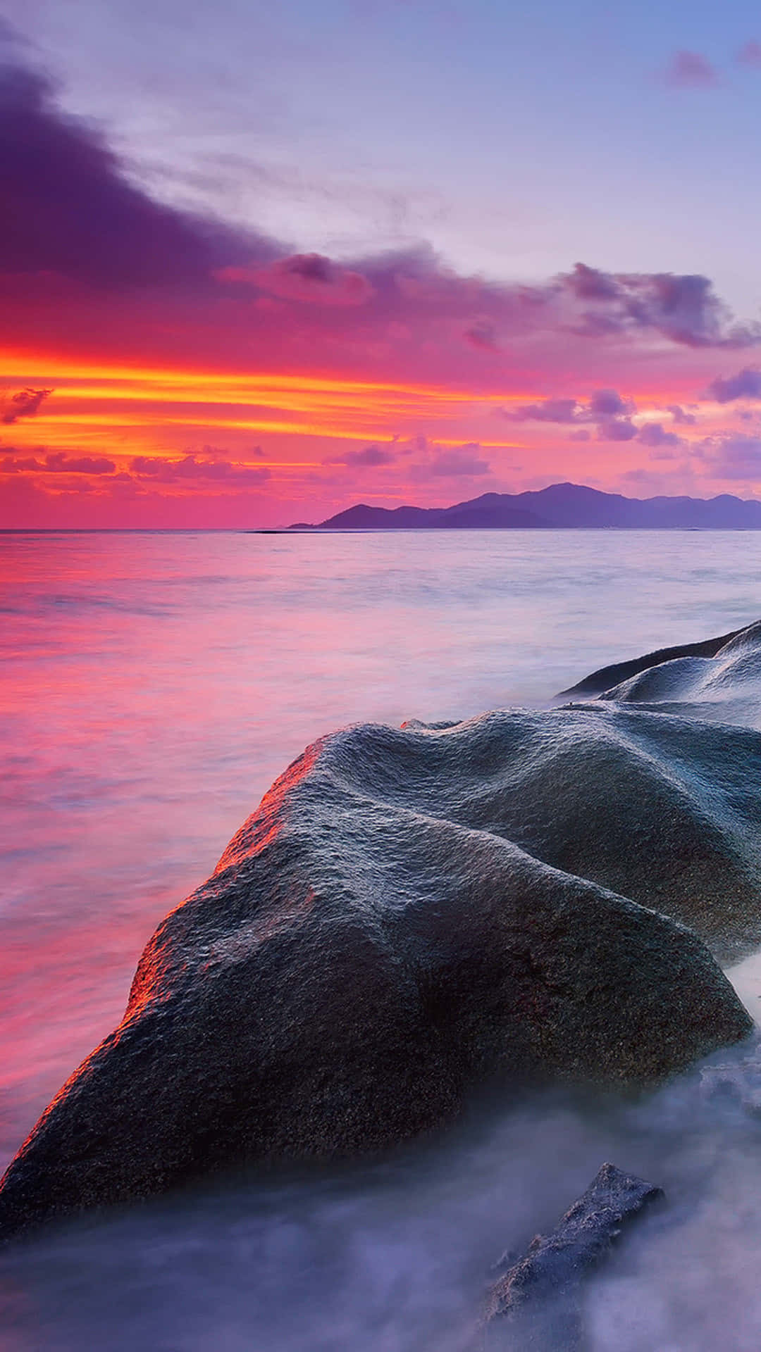 A Sunset Over A Beach With Rocks And Water Background