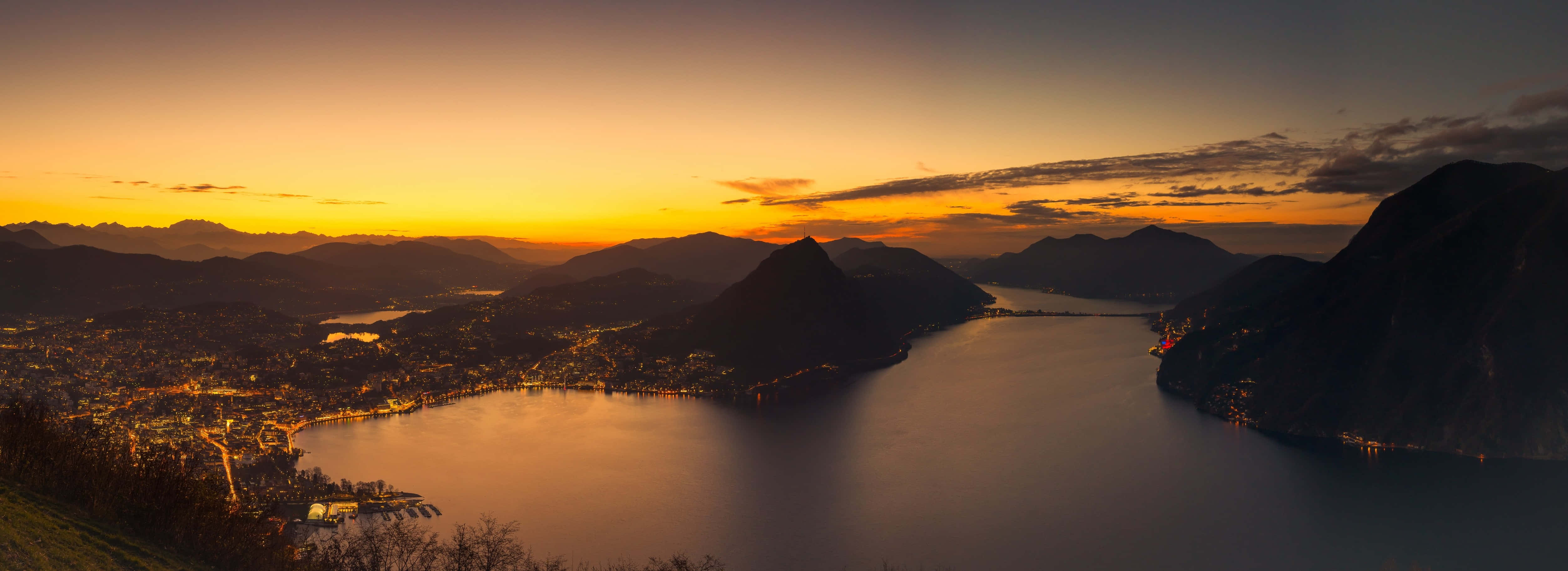 A Sunset Over A Lake And Mountains