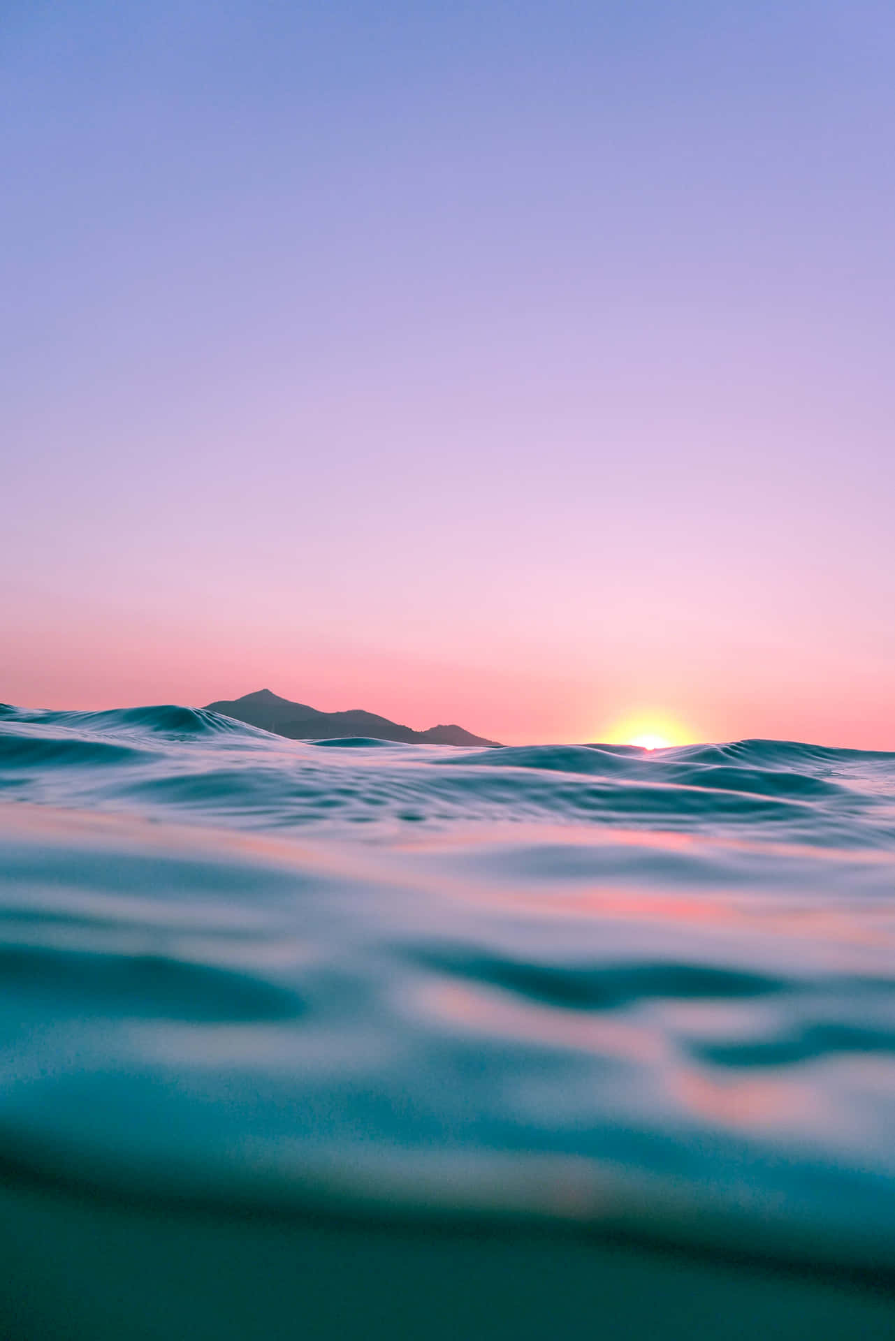 A Sunset Over The Ocean With Waves And Mountains Background