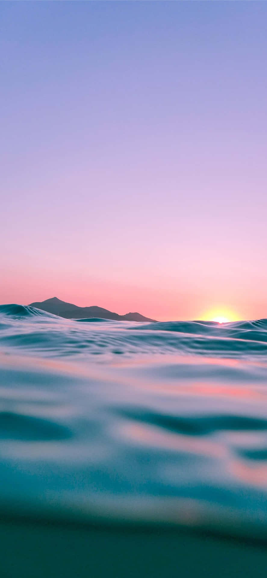 A Sunset Over The Ocean With Waves And Mountains Background