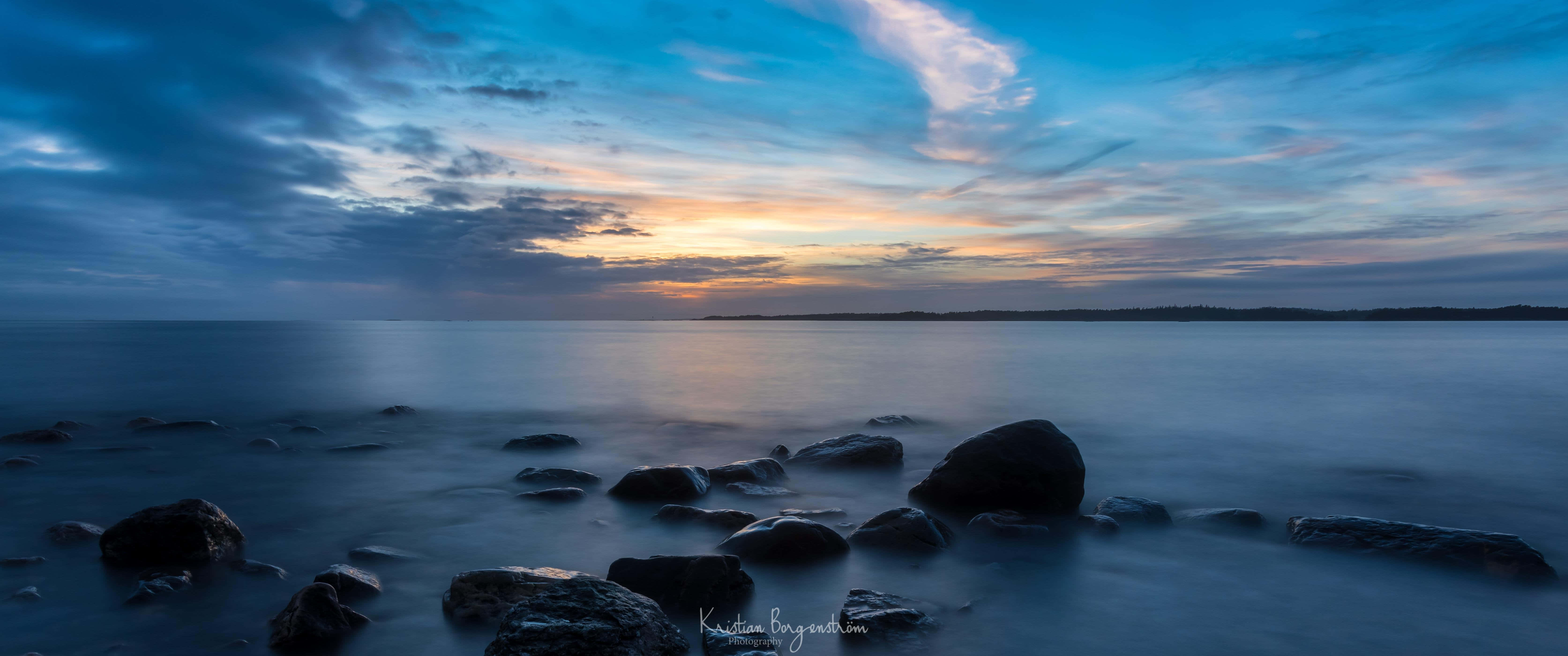 A Sunset With Rocks And Water In The Background Background