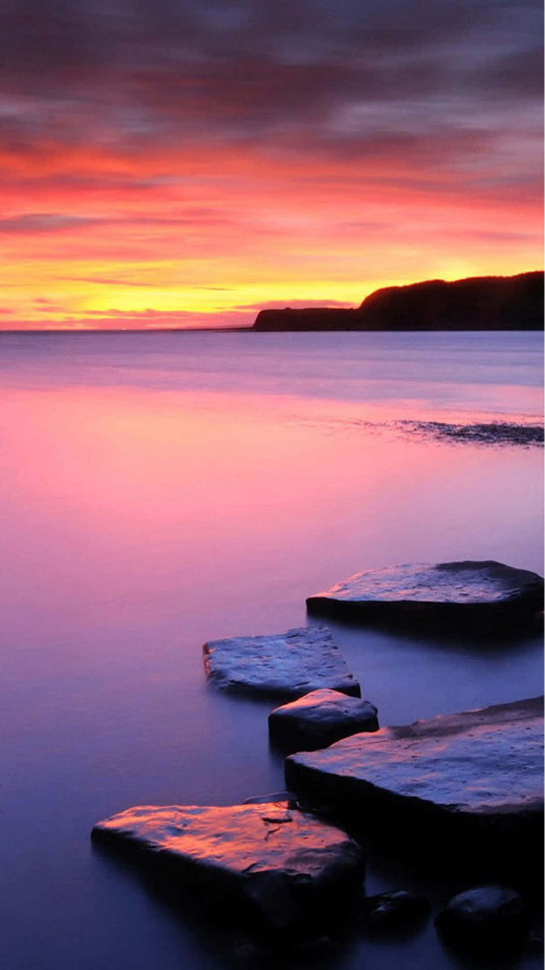 A Sunset With Rocks In The Water Background