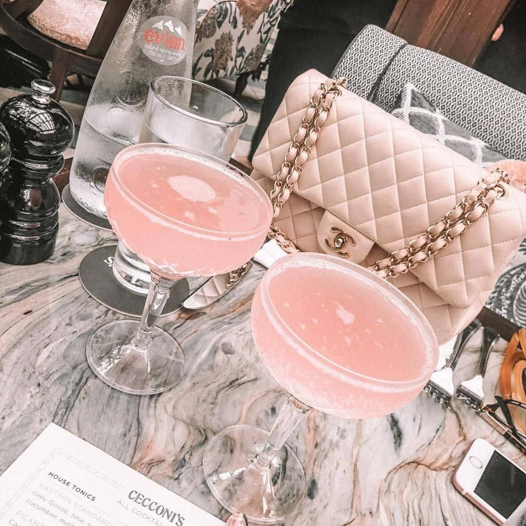 A Table With Two Pink Drinks And A Purse Background