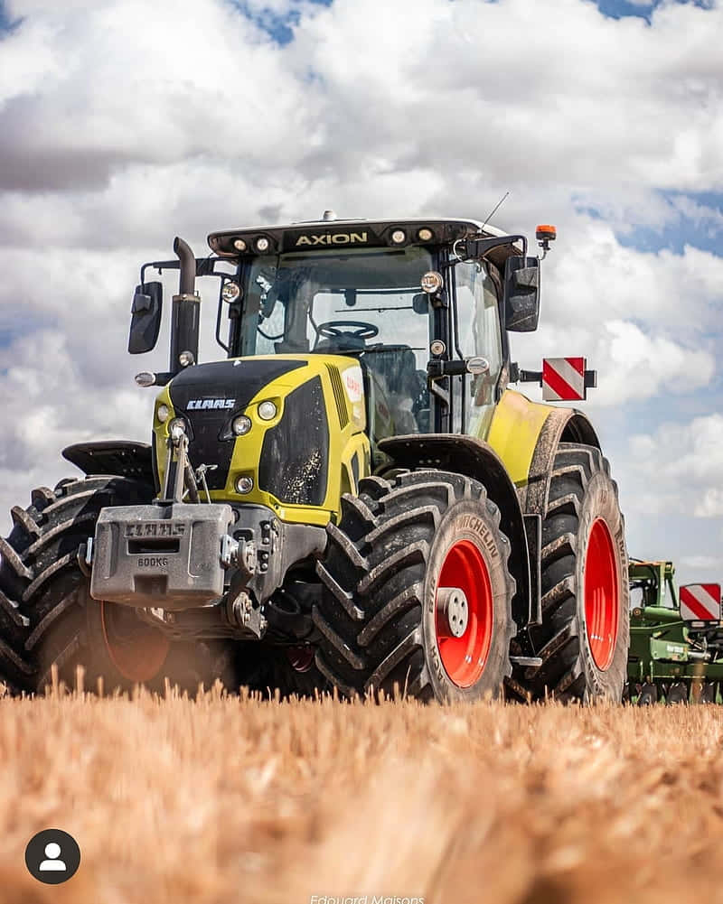 A Tractor Driving Through A Field With A Cloudy Sky Background