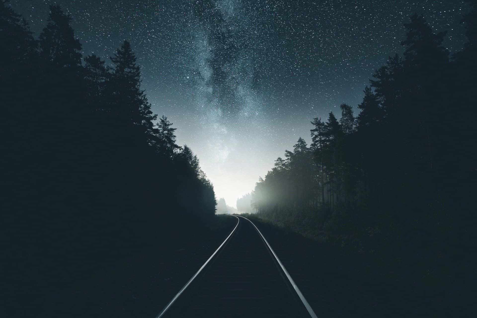 A Train Tracks In The Forest With The Stars Above Background
