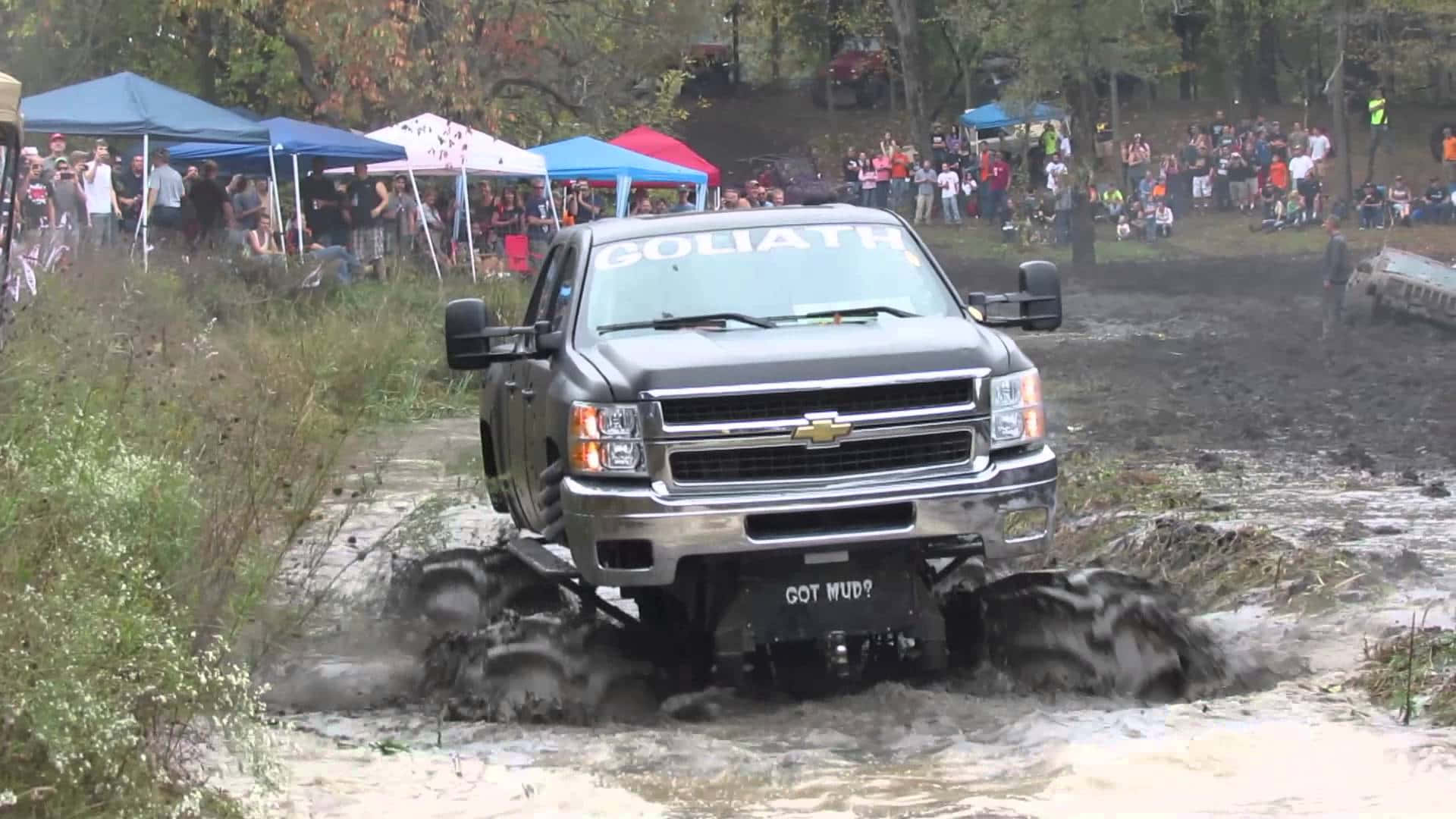 A Truck Driving Through Mud At A Festival Background