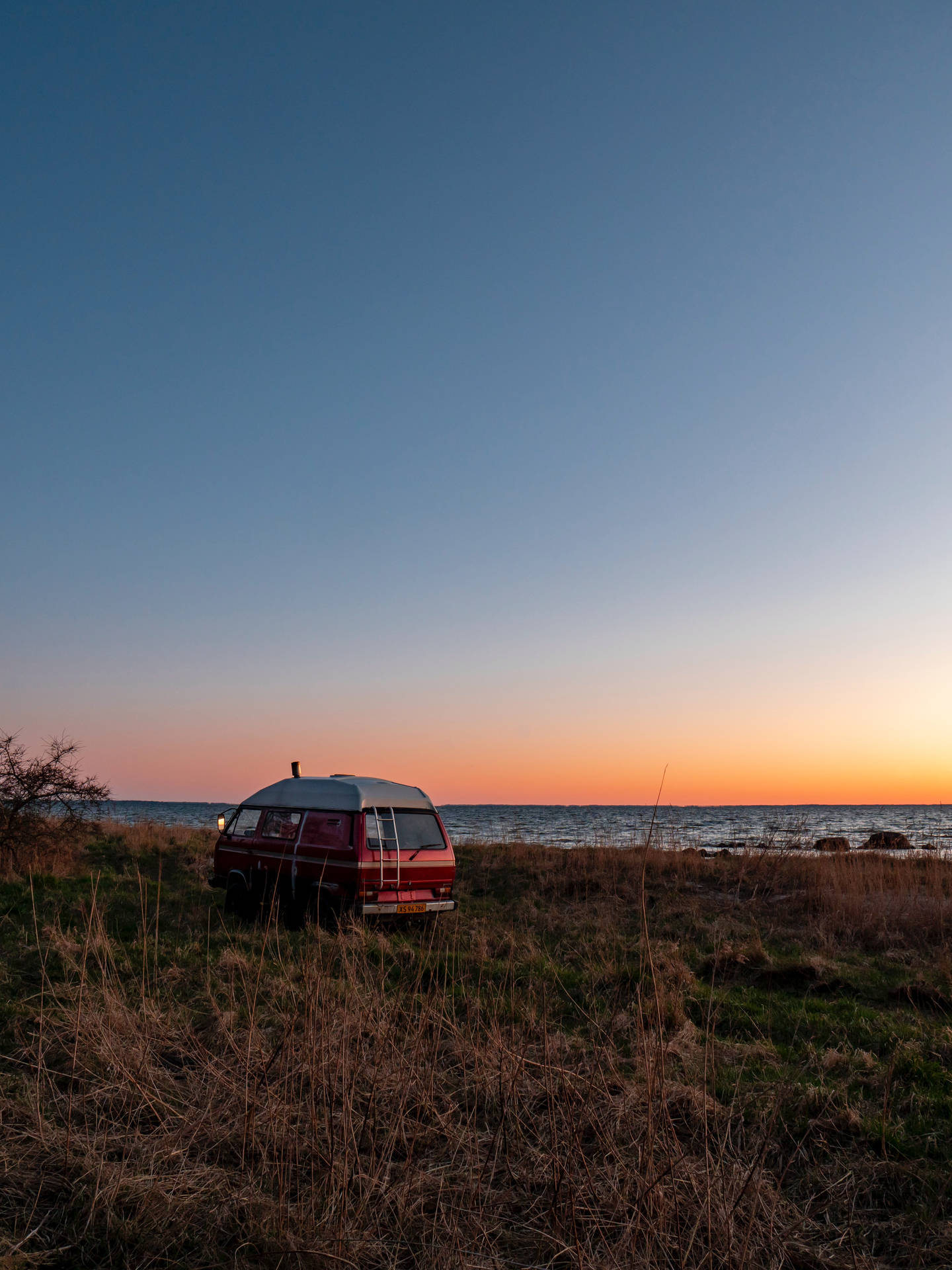 A Van Parked In A Field Near The Ocean Background