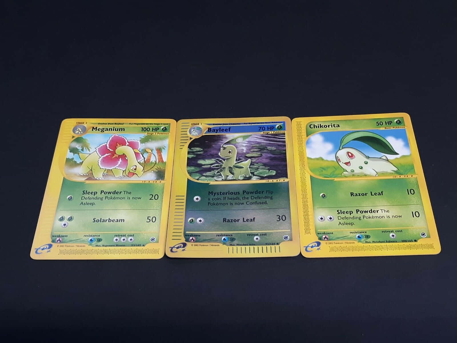 A Vibrant Depiction Of Meganium, Bayleef, And Chikorita In Pokémon Trading Cards Background